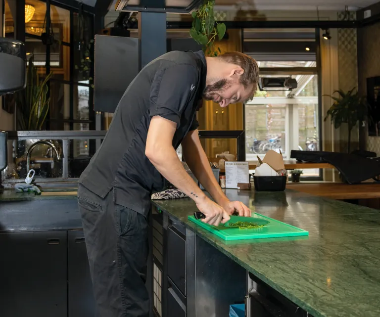 Kitchen worker taller than 1.80 m cutting hunched over at a worktop that is too low